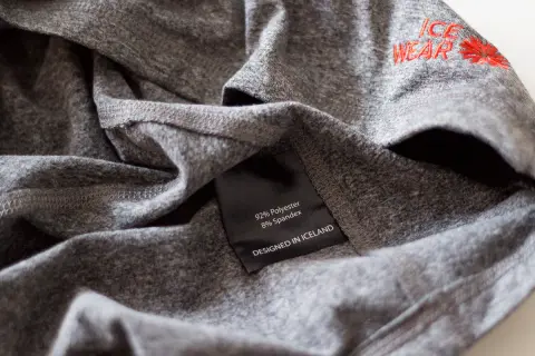 Szara koszulka z metką: 92% poliester, 8% spandex. Poliester co to za materiał? Wytrzymały i szybkoschnący, idealny do odzieży sportowej.