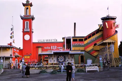 Färgglatt lustiga huset med torn och rutschkana. Folk minglar vid bar och kaffe.
