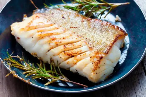 Zdrowa ryba zębacz, soczysty filet z chrupiącą skórką, podany z rozmarynem na talerzu.