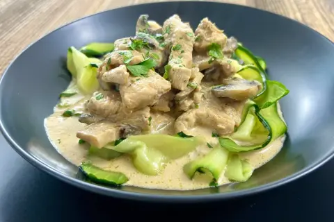Pyszny keto obiad: kurczak w sosie śmietanowo-grzybowym z cukinią w kształcie wstążek, posypany natką pietruszki.