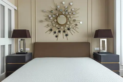 Un espejo sol y lámparas oscuras sobre mesitas de noche grises ayudan a alegrar una habitación con muebles oscuros.