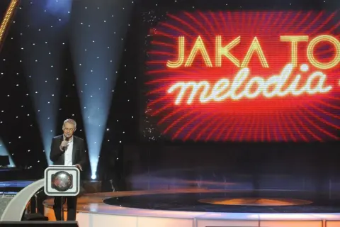 Prowadzący w studiu "Jaka to melodia?" z mikrofonem. Zastanawiasz się, ile kosztuje minuta reklamy w trakcie trwania tego programu?