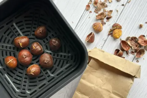 Châtaignes grillées dans un air fryer, prêtes à être dégustées. Les peaux éparpillées témoignent de leur préparation facile.
