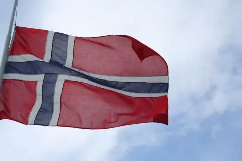 Flaga Norwegii powiewa na wietrze na tle błękitnego nieba z chmurami.