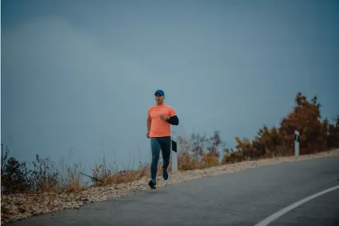 Mężczyzna w pomarańczowej koszulce i czapce biega po pustej drodze. Czy można biegać na czczo? To pytanie zadaje sobie wielu sportowców.
