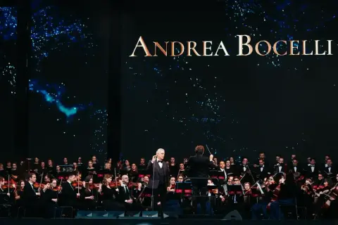 Andrea Bocelli koncert 2026. Wokalista śpiewa z orkiestrą symfoniczną na tle gwieździstego nieba.