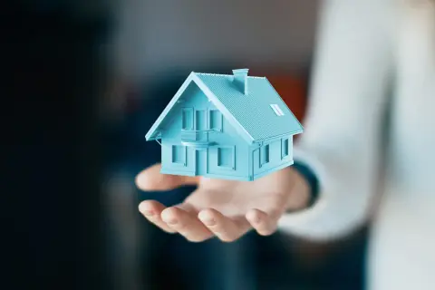 Dłoń trzyma błękitny model domu. Czy to darowizna? Co to znaczy?