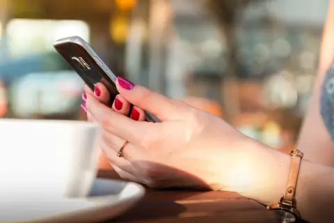 Kobieta z pomalowanymi paznokciami trzyma telefon, szukając informacji, jak zmienić dźwięk powiadomień w Messengerze.