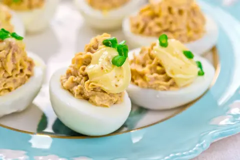 Pyszne jajka faszerowane tuńczykiem, udekorowane majonezem i szczypiorkiem, podane na ozdobnym talerzu.