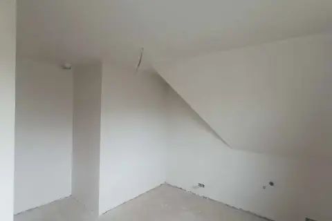 Wnętrze pokoju ze skośnym sufitem, ściany pokryte tynkiem gipsowym bez gładzi, gotowe do malowania.