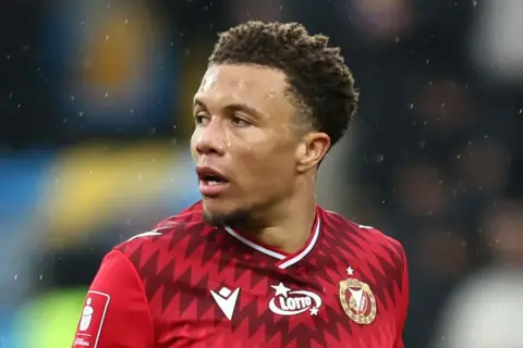 Piłkarz Rakowa Częstochowa w czerwonej koszulce z logo Lotto, gotowy do gry przeciwko Widzewowi Łódź.