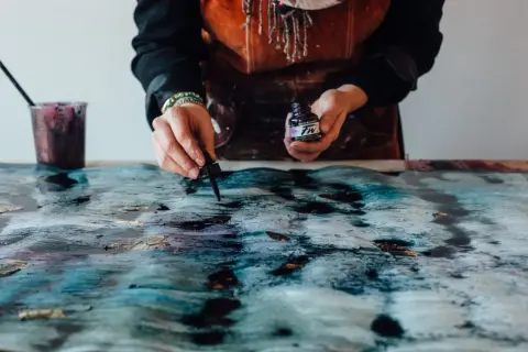 Manos aplicando tinta a un lienzo texturizado, como enmarcar un lienzo con arte abstracto.