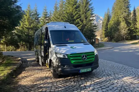 Nowy, ekologiczny bus na Morskie Oko czeka na turystów. W tle góry i las.