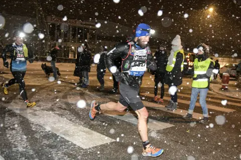 Coureurs de la SaintéLyon affrontant la neige. Un homme porte une lampe frontale et un dossard "Asics".