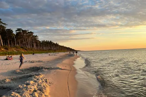 Piękny zachód słońca na plaży w Choczewie. Ludzie spacerują, a morze delikatnie faluje.