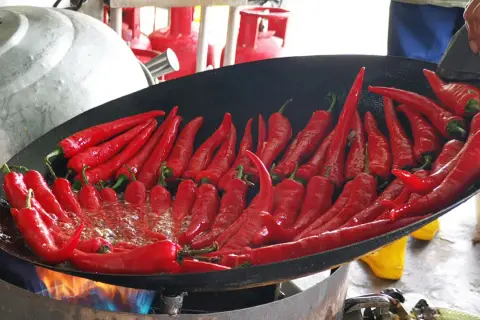 Viele rote Chilis brutzeln in einer Pfanne über offenem Feuer. Wenn der Chili zu scharf ist, was tun? Vielleicht mehr Öl hinzufügen?