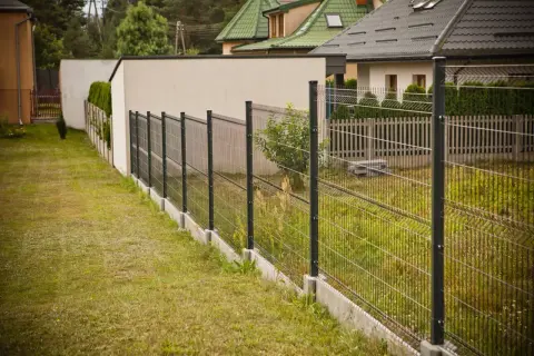 Nowoczesne ogrodzenie działki z siatki i paneli, biegnące wzdłuż trawnika i domów.