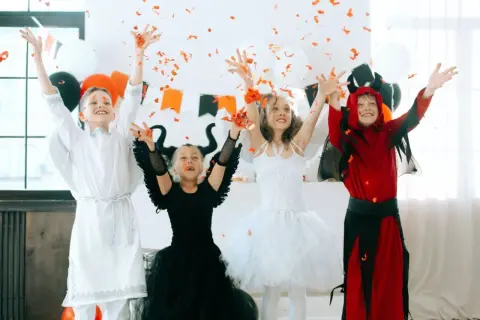 Dzieci w strojach aniołów i diabła rzucają konfetti. Inspiracja, jak zrobić strój na Halloween dla dziecka.