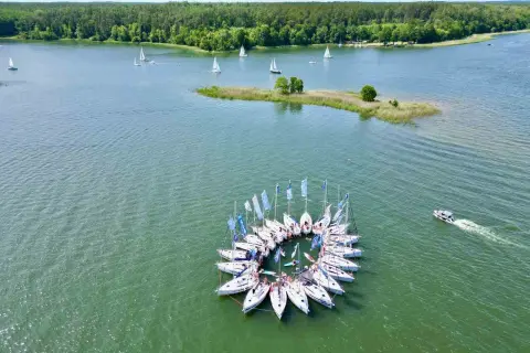 Żeglarska feta na Mazurach! Jachty tworzą krąg, a w tle las i jezioro. Idealne miejsce, by zapytać: gdzie na Mazury?