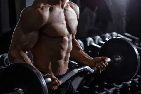 Uomo muscoloso in palestra esegue curl con bilanciere. Quante serie per gruppo muscolare sono necessarie per ottenere un fisico scolpito come questo?