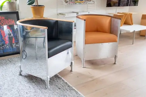 Två fåtöljer i källemo aluminium med svarta och orange lädersitsar. En spegelblank yta reflekterar rummet.