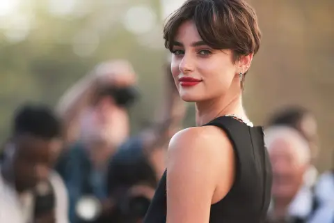 Mujer con un moderno corte bixie, labios rojos y mirada intensa, rodeada de fotógrafos.
