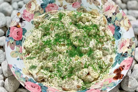 Enkel potatissallad med krämig crème fraiche, toppad med färska örter. Serveras i en vacker skål med blomstermönster.