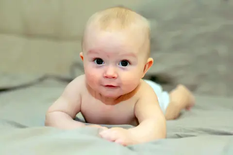 Bebé boca abajo, con los brazos apoyados, mostrando el reflejo de enderezamiento en su mirada curiosa.