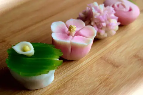 Délicates pâtisseries japonaises en forme de fleurs et de calla, aux couleurs pastel, sur fond de bois.