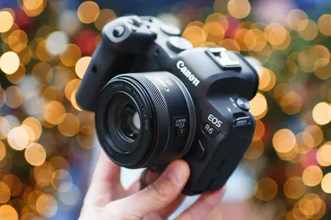 Dłoń trzyma aparat Canon EOS R6 z obiektywem 50 mm f/1.8 STM na tle świątecznych światełek.