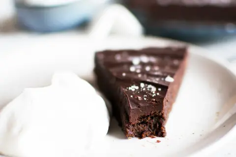 En bit vegansk kladdkaka med en klick vispad grädde, strödd med flingsalt.