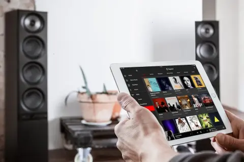 Mann sucht auf einem Tablet nach neue Musik. Im Hintergrund stehen zwei schwarze Lautsprecher.