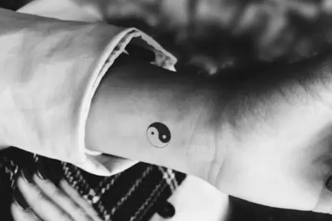 Delikatny tatuaż symbolizujący ogień i wodę, yin i yang, na nadgarstku.