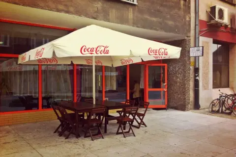 Tanie jedzenie Wrocław Rynek: stoliki pod parasolem Coca-Cola, wejście do lokalu, rowery przy ścianie.
