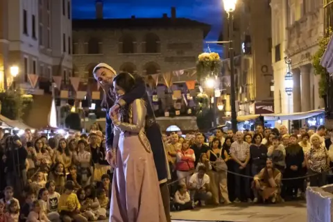 Una pareja se abraza en una calle iluminada por farolas, ante una multitud que observa. Podría ser la escena de "la partida de Diego".