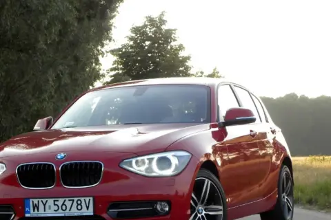 Czerwone BMW 118d na tle drzew i pól.