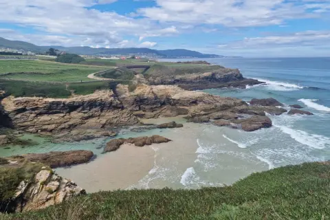 Senderistas disfrutan de las impresionantes rutas senderismo Foz, con acantilados rocosos, playas de arena y el mar azul.