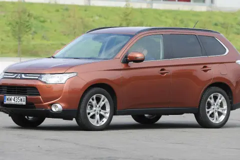 Brązowy Mitsubishi Outlander 3 na tle zielonego wzgórza.