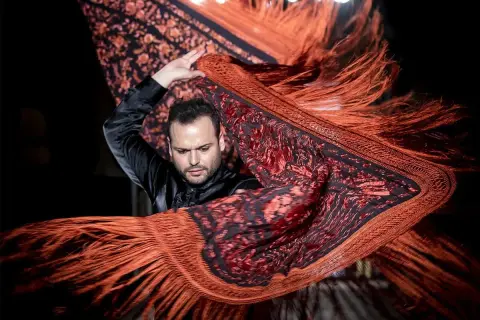 Un bailarín flamenco agita un mantón de Manila de origen oriental, con flecos anaranjados y estampado floral.