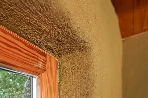Lehmputz nachteile: raue Textur, die Schmutz anziehen kann, um ein Fenster mit Holzzarge und sichtbarem Putz.