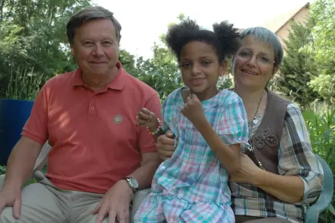 Un homme, une femme et une petite fille souriants, peut-être la famille de Leonard Berducat, profitent d'un moment ensoleillé dans un jardin.