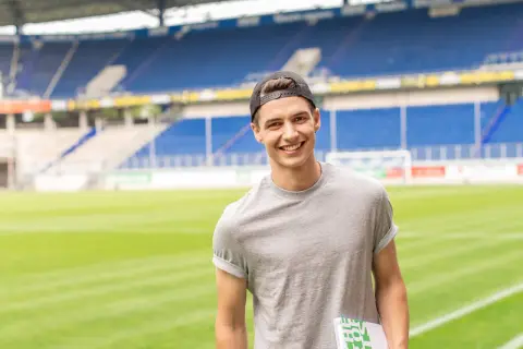 Junger Mann mit Kappe und Buch im Stadion, bereit für seinen Eventmanagement Master.