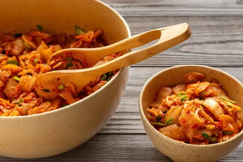 Två skålar med kryddig, fermenterad mat, troligen kimchi, med träskedar i den större skålen.