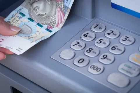 Dłoń wkłada banknot 500 zł do bankomatu. Zastanawiasz się, mbank ile idzie przelew?