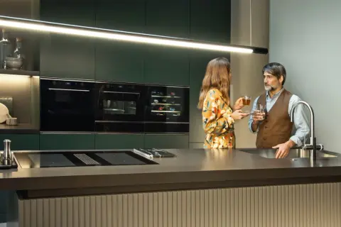 Para w nowoczesnej kuchni, przy wyspie z płytą indukcyjną i zintegrowanym okapem, delektuje się napojami.