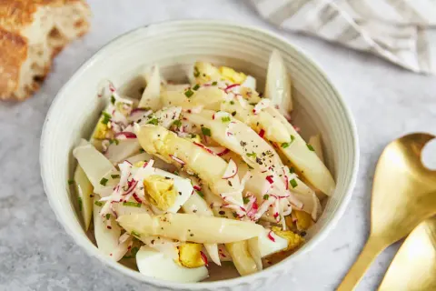 Schüssel mit Spargelsalat mit Ei, Radieschen und Schnittlauch, dazu ein Stück Baguette.
