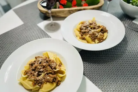Deux assiettes de pâtes conchiglioni garnies d'une généreuse sauce bolognaise, prêtes à être dégustées avec un verre de vin rouge.