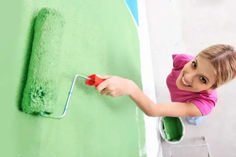 Frauen streichen bei Auszug nach 5 Jahren die Wand grün. Sie lächelt fröhlich, während sie mit der Rolle die Farbe aufträgt.