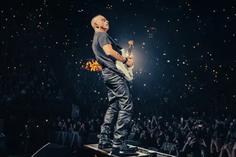 Eros Ramazzotti gra na gitarze podczas koncertu, a tłum w ciemnościach trzyma zapalone telefony.