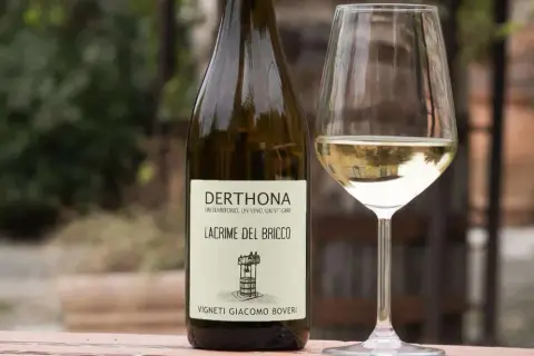 Calice e bottiglia di Derthona, vino Timorasso. Le caratteristiche di questo vino bianco piemontese sono freschezza e note minerali.